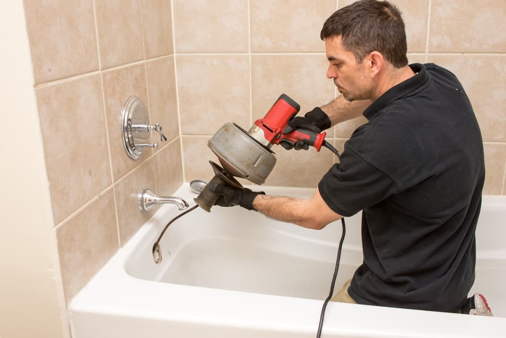 plumber unclogging shower drain with tools.