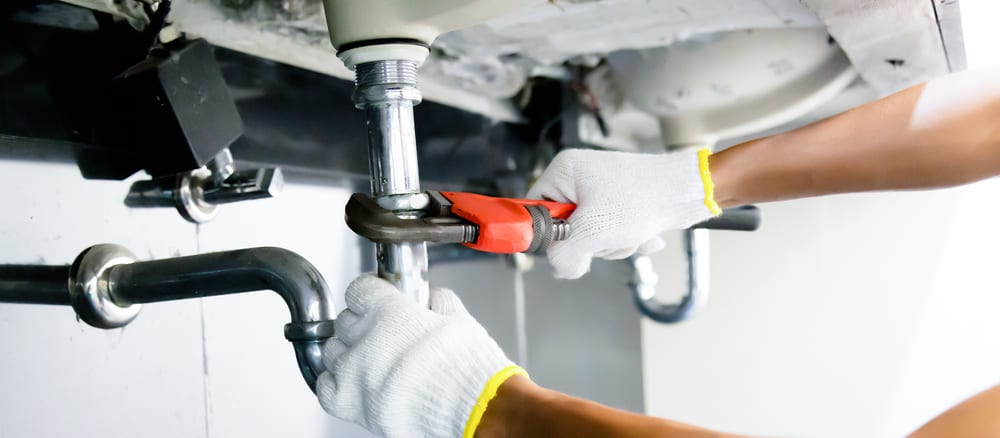 Leak repair plumbing professional working on pipe fittings, commercial plumbing services, New York.