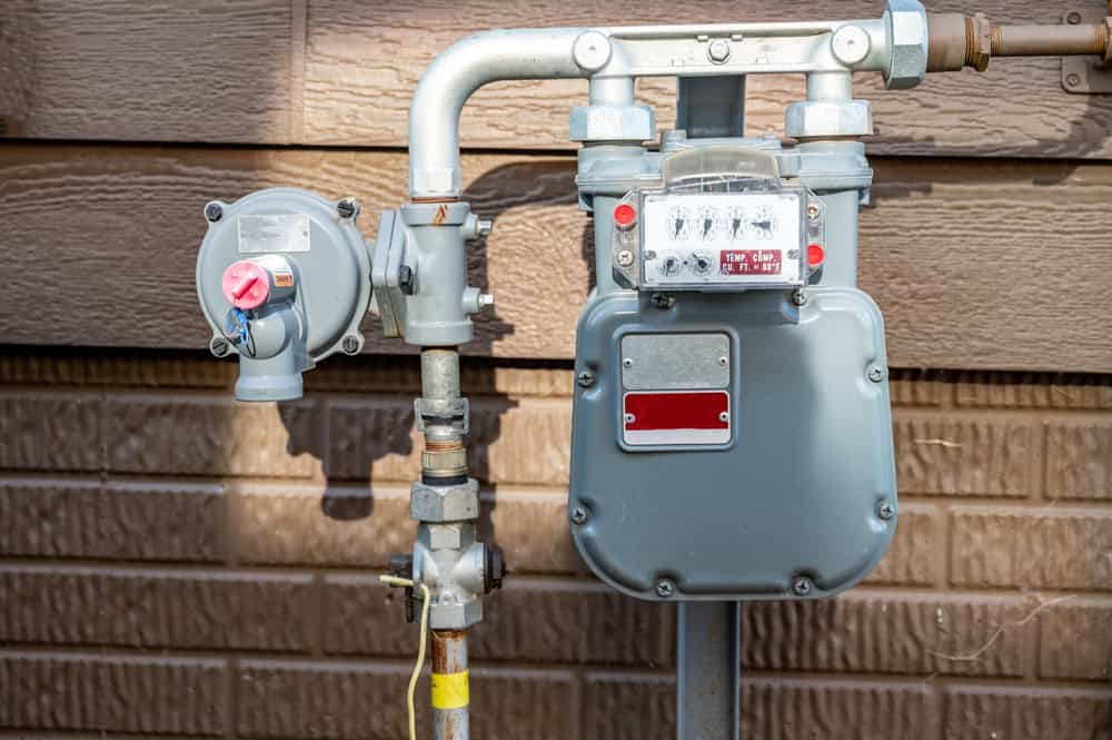 Gas meter for natural gas service, essential plumbing and heating equipment, on exterior wall of home.