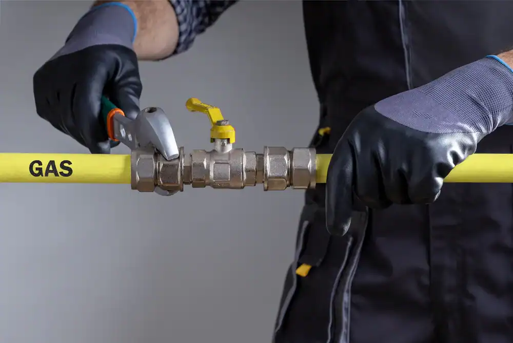 A person wearing black gloves uses a wrench to tighten a metal valve on a yellow gas pipe labeled "GAS.