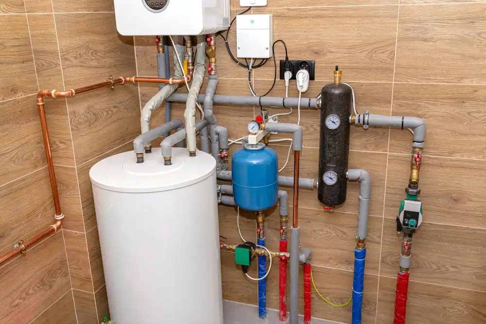 Home boiler room with a white water heater, blue expansion tank, various pipes, valves, pressure gauges, and control devices mounted on wood-patterned tiled walls.